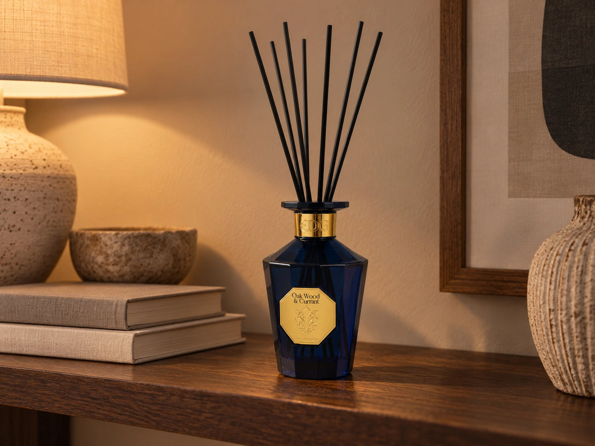 EDG Gold Lily Oak Wood & Currant duftpinner på en mørk trehylle med bøker og varm belysning
